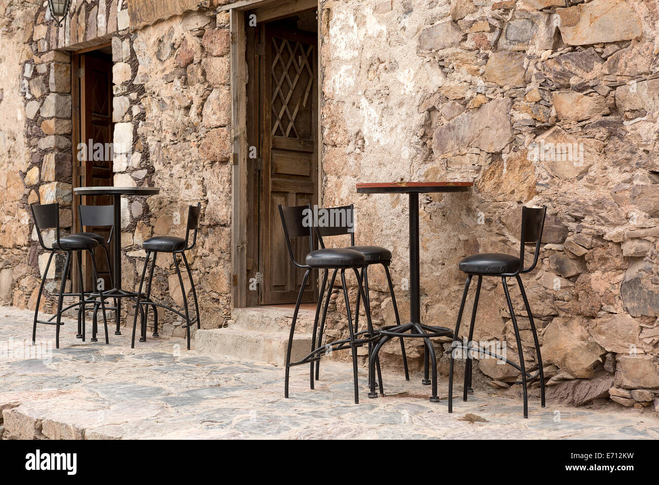 high bar stools and tables in the front of a rustic restaurant building