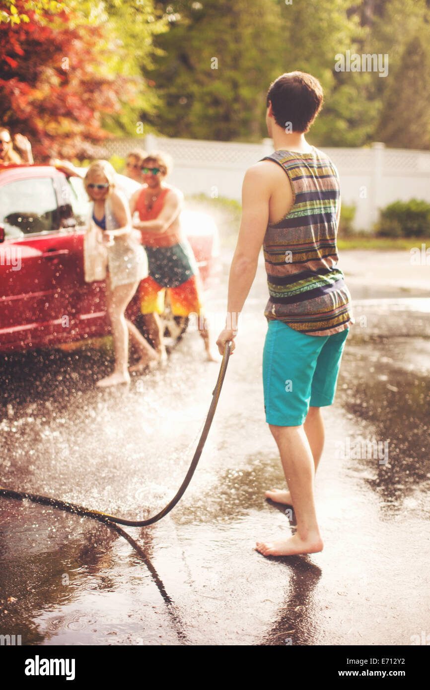 Young man spraying friends with hosepipe Stock Photo