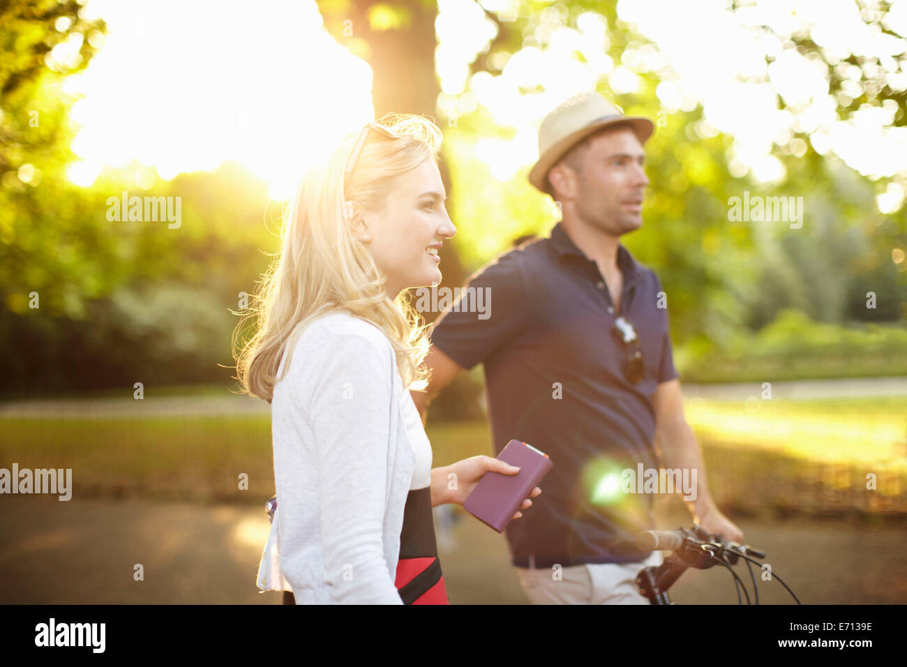 Couple with bicycle strolling in sunlit park Stock Photo