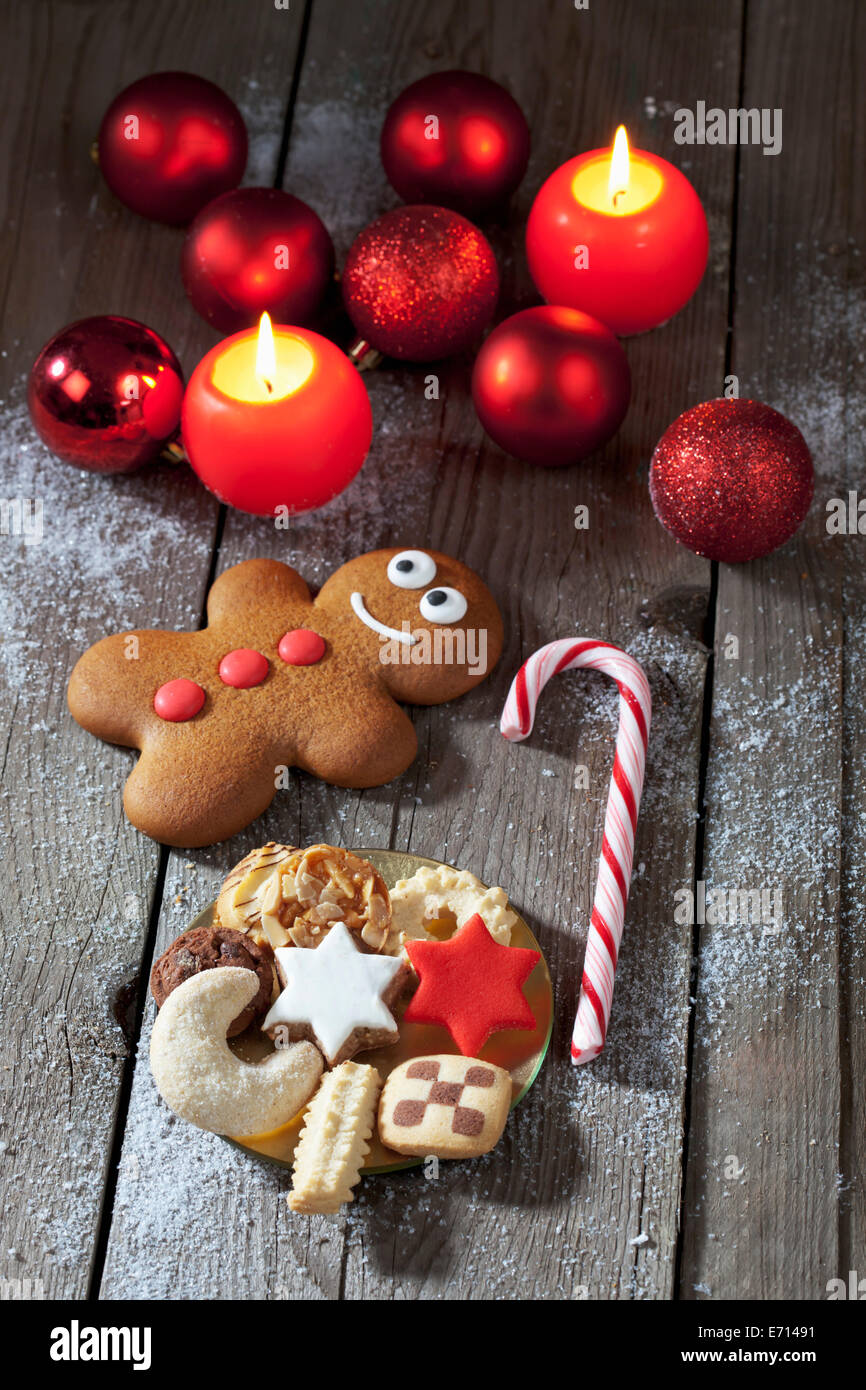 Gingerbread man, sugar cane, plate of Christmas cookies, Christmas baubles and lighted candles on grey wood Stock Photo