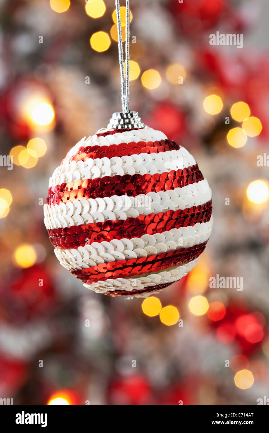 Christmas bauble decorated with red and white sequins hanging in front of blurred flares Stock Photo