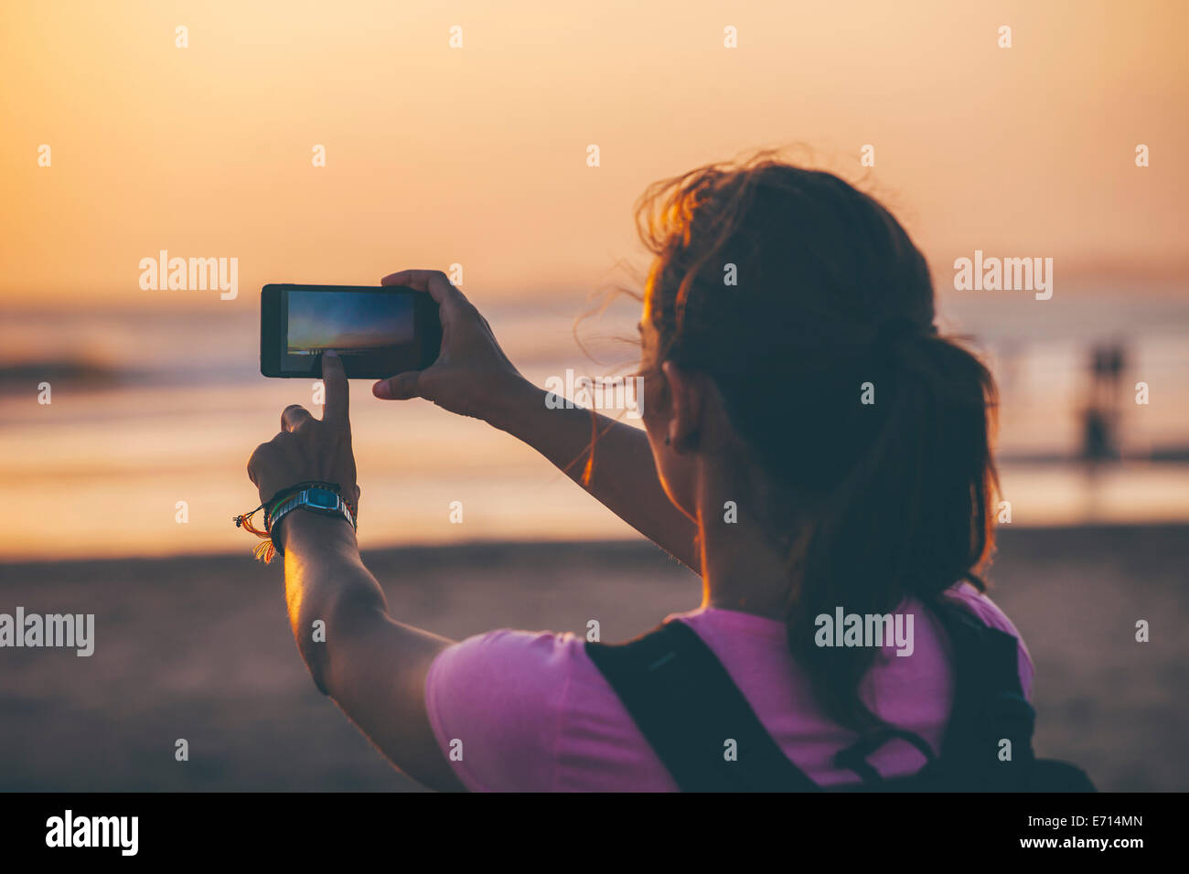 Indonesia, Bali, woman on the beach photographing sunset with her smartphone Stock Photo