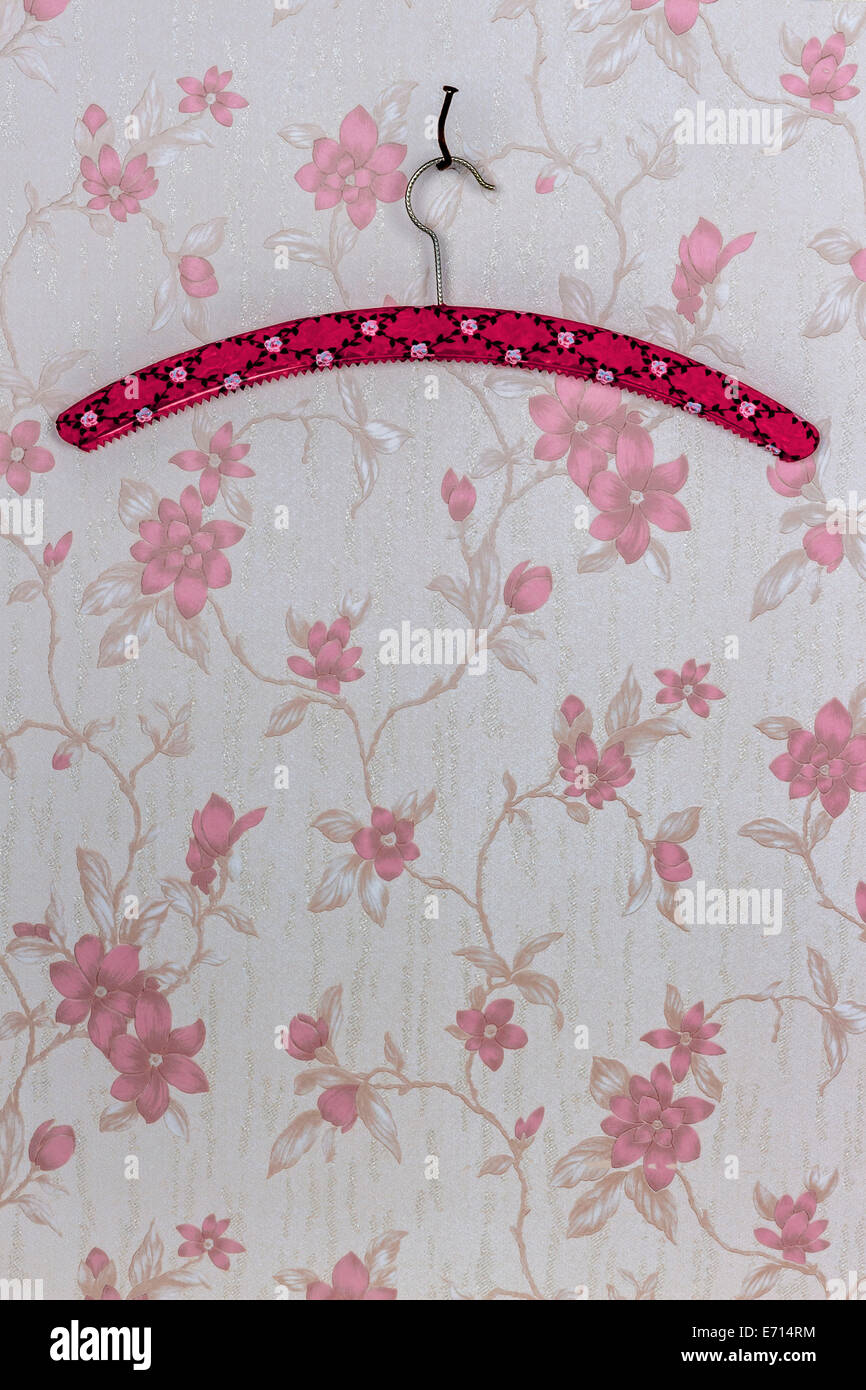 Clothes hanger fixed with a bent nail hanging on wallpaper with pink floral design Stock Photo