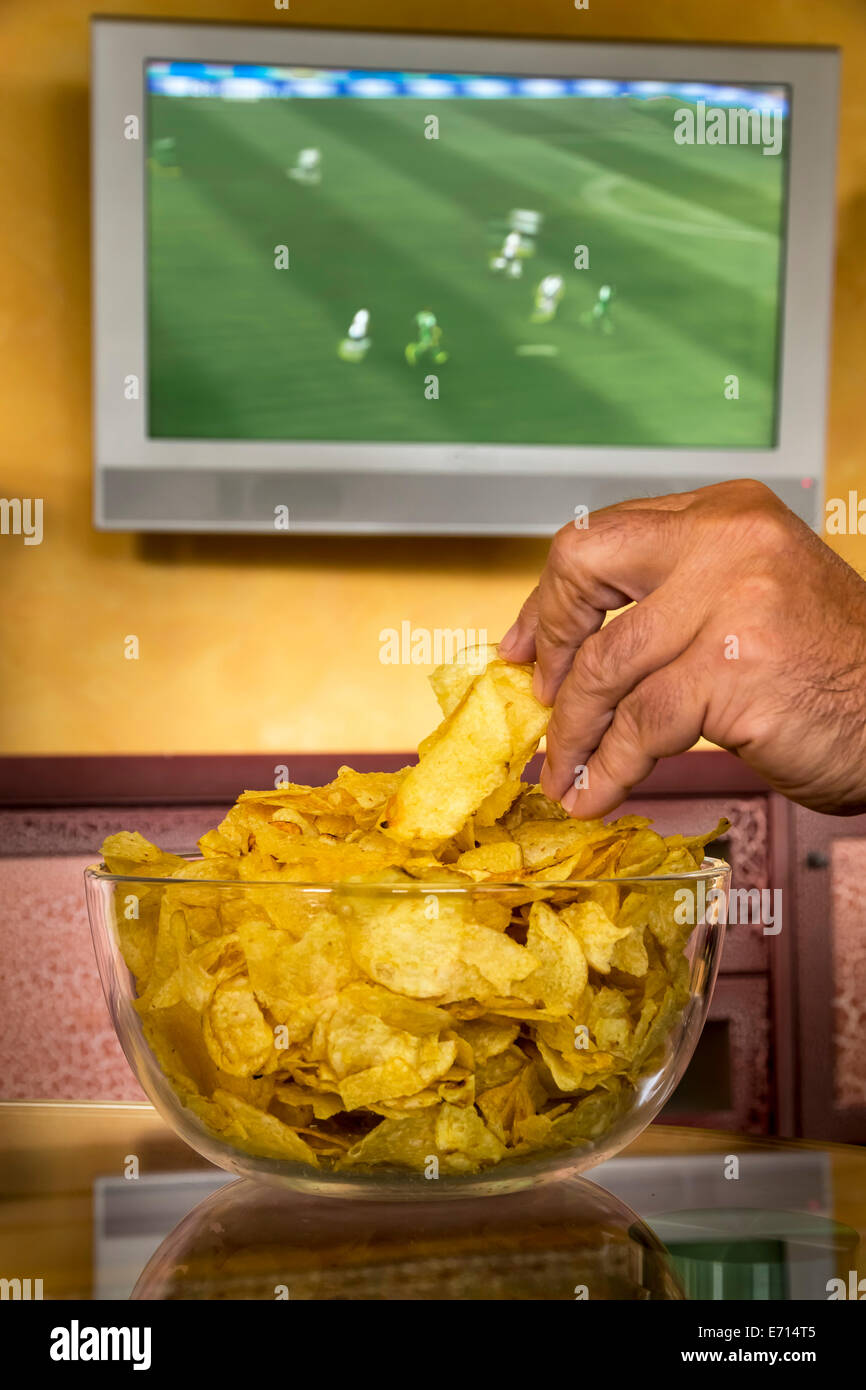 Man's hand taking potato chips from a glass bowl in front of flatscreen
