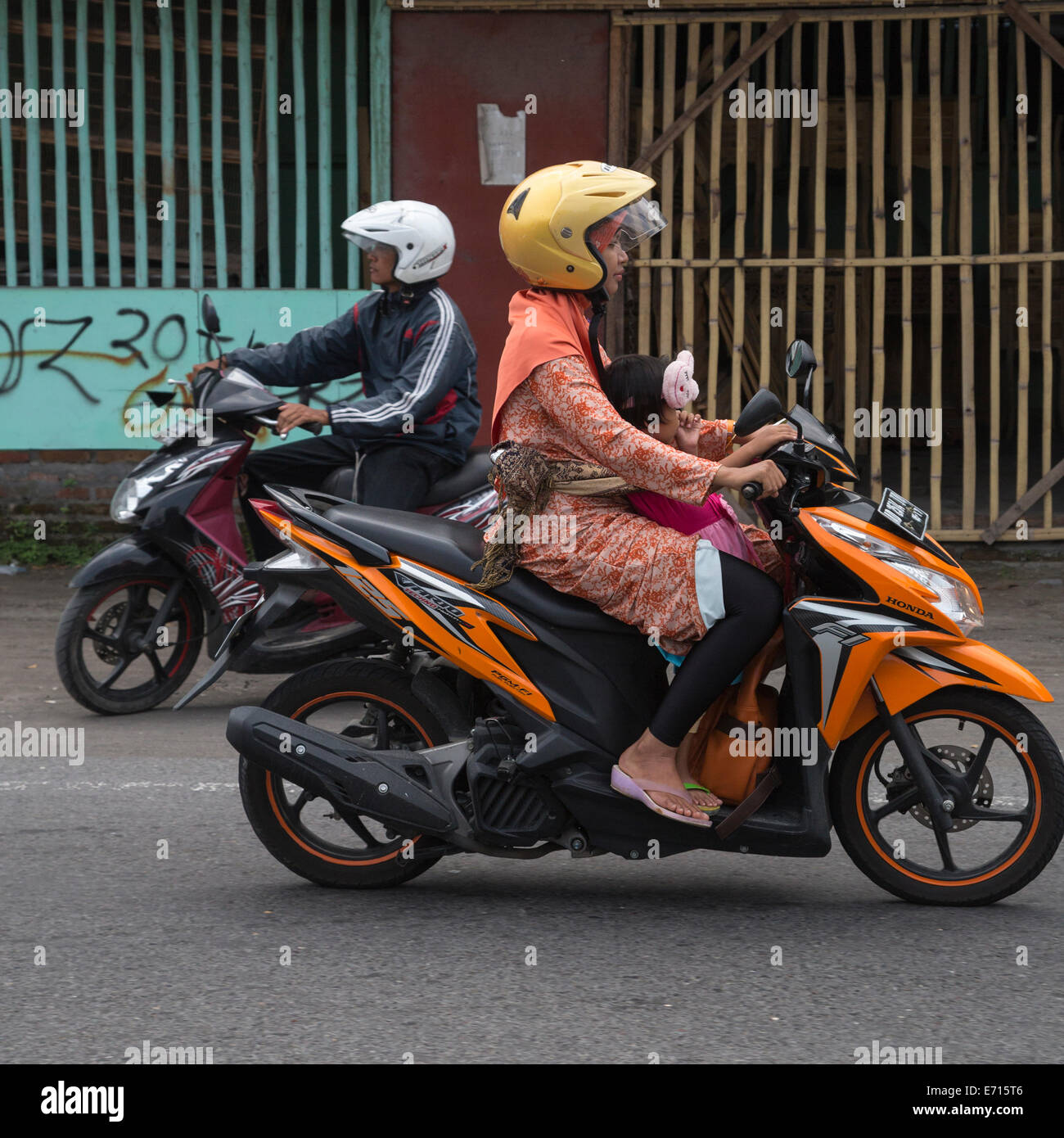 Yogyakarta, Java, Indonesia.  Road Safety.  Little Girl Sucking her Thumb while Riding with her Mother on a Motorbike. Stock Photo