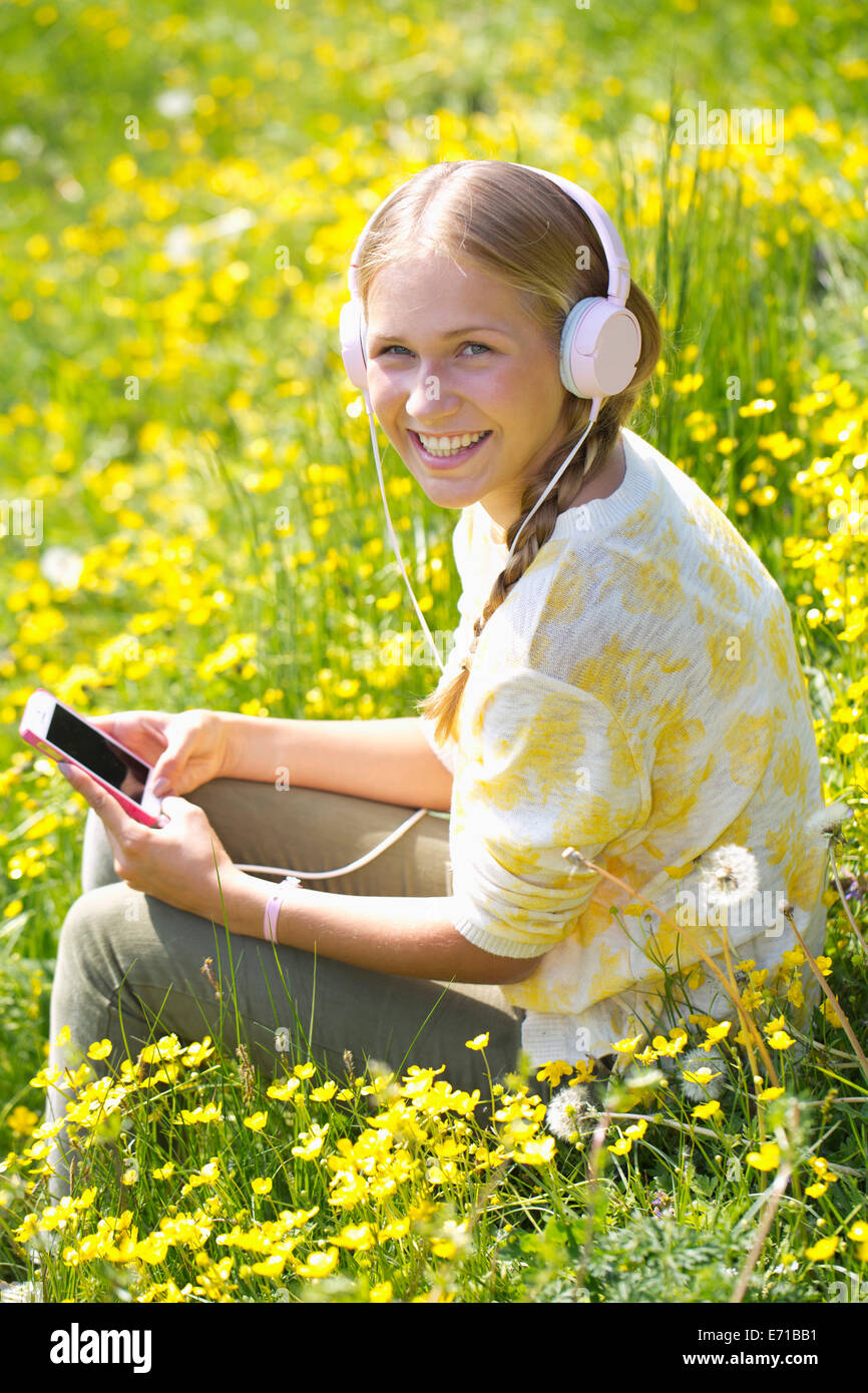 Portrait of smiling teenage girl with headphones hearing music on a flower meadow Stock Photo