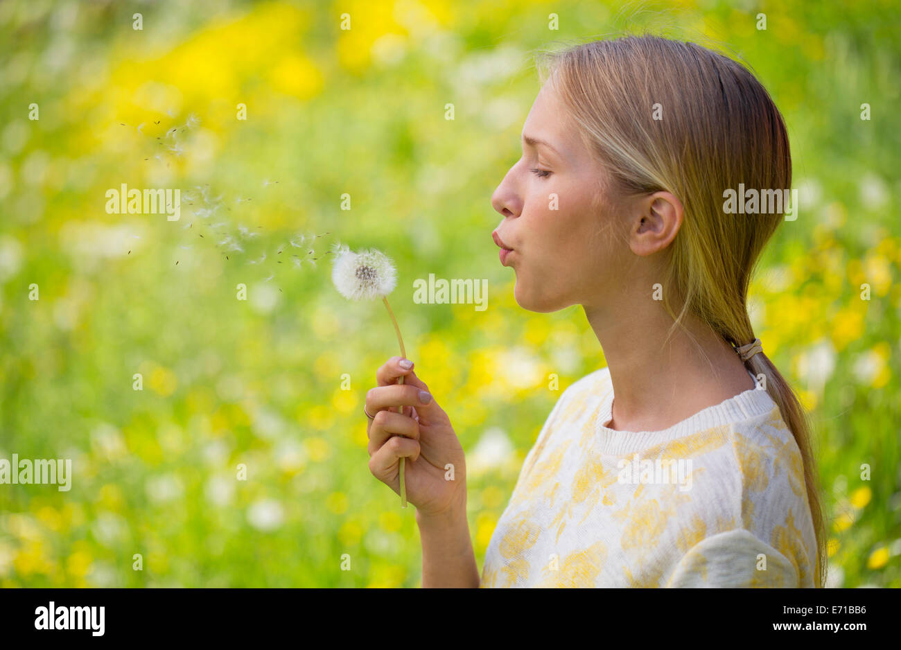 Portrait of teenage girl blowing blowball on a flower meadow Stock Photo