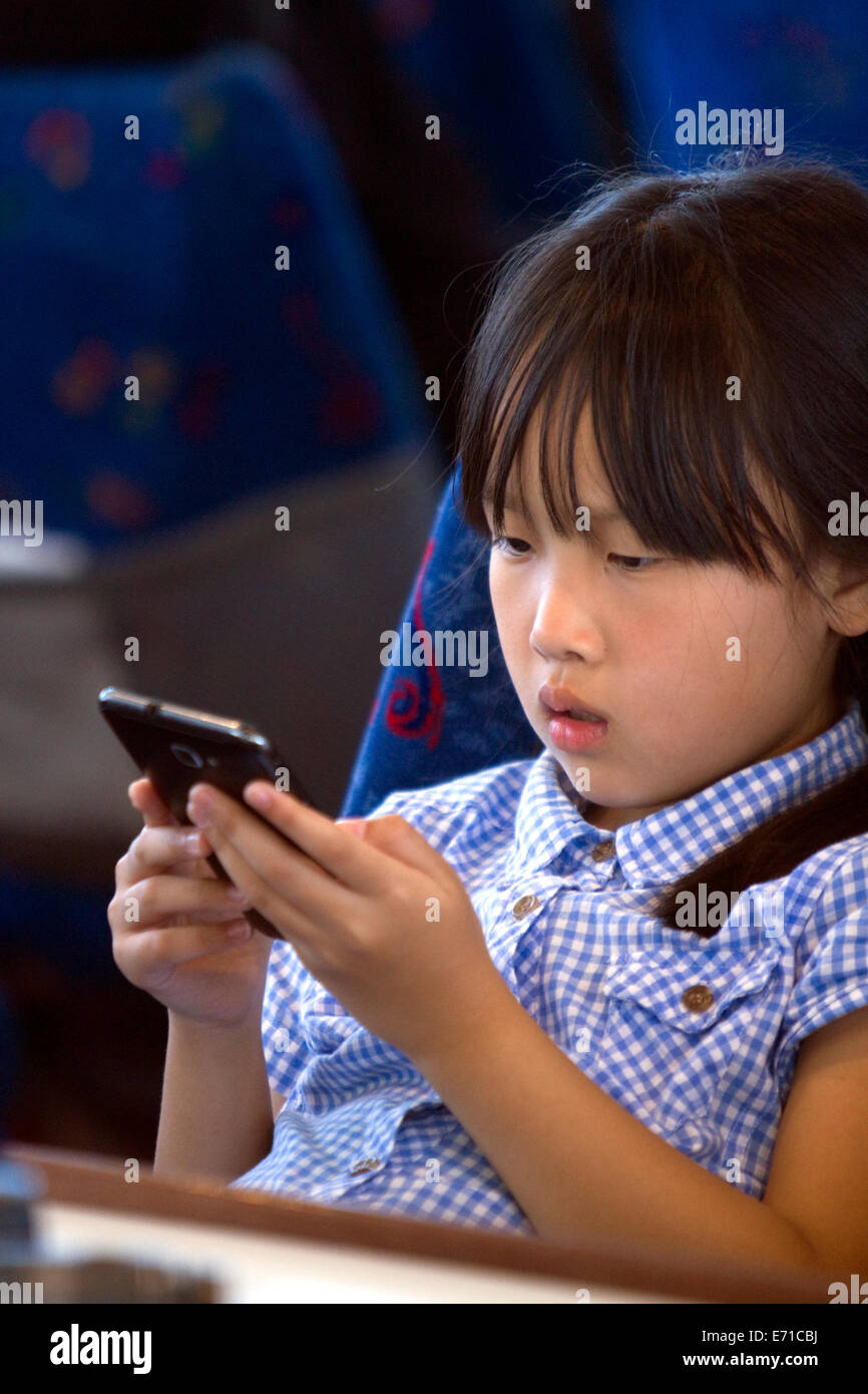 Asian girl playing with a smart phone while on a tour boat in the Bay of Islands, North Island, New Zealand. Stock Photo