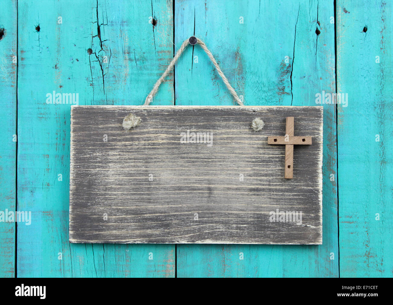 Weathered blank sign with wooden cross hanging on antique teal blue rustic wood door Stock Photo