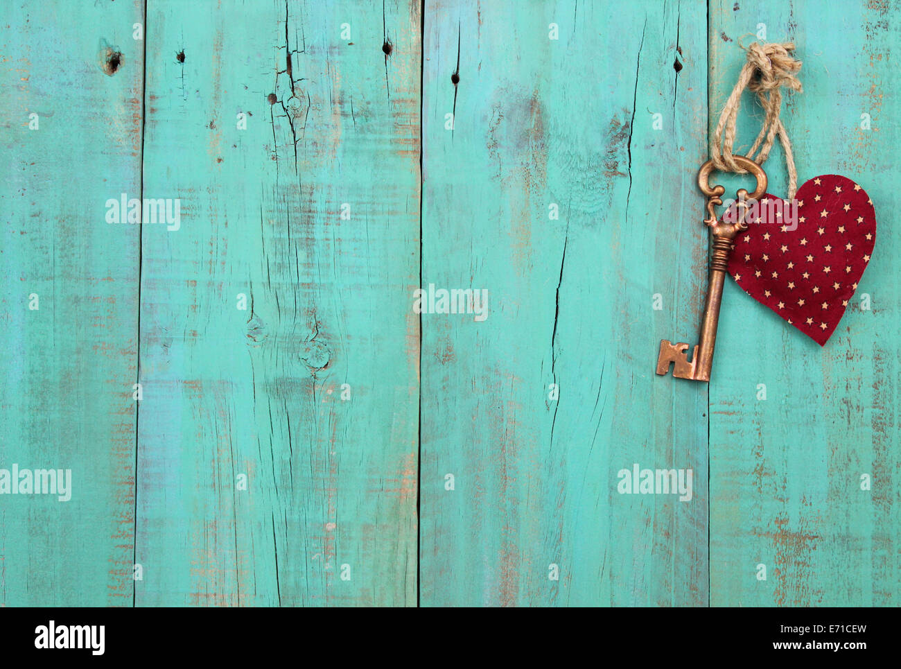 Bronze skeleton key and red heart hanging from rope on antique green distressed wood door Stock Photo