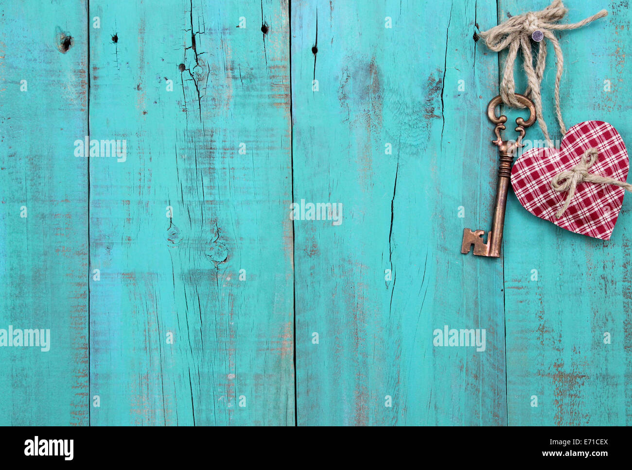 Bronze skeleton key and red checkered heart hanging from rope on antique green rustic wood door Stock Photo