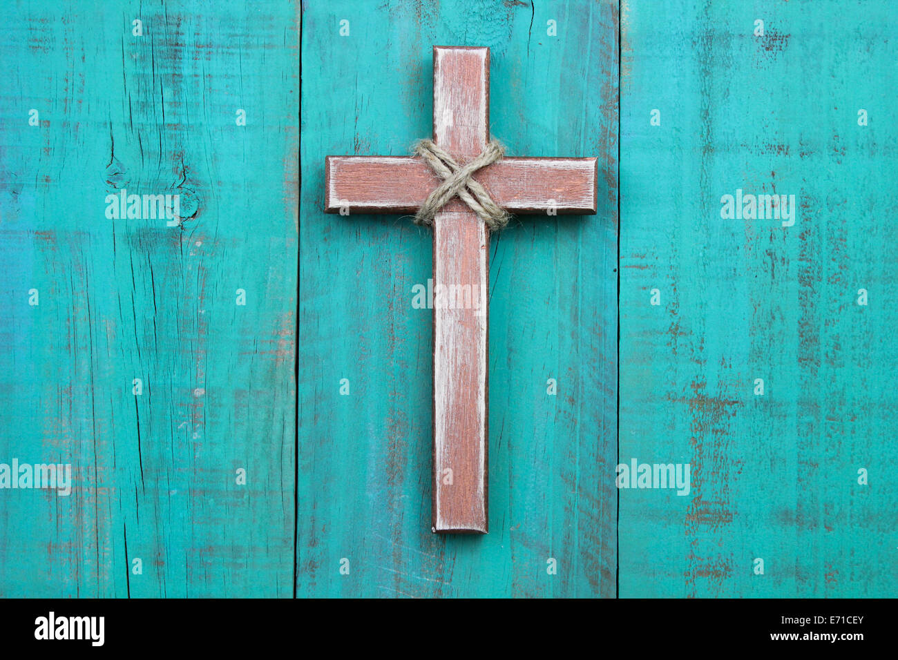 Rugged wooden cross hanging on antique teal blue rustic wood background Stock Photo