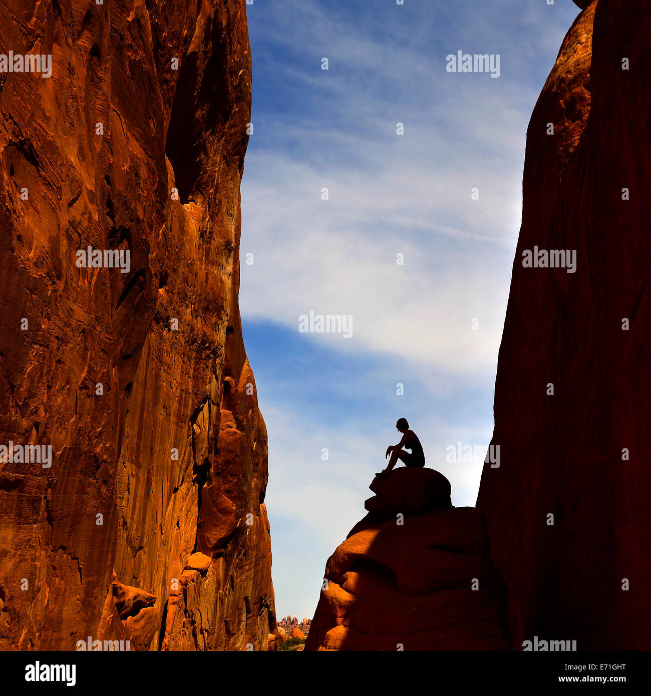 Silhouette of woman sitting on stone in rock canyon in Arches National Park Stock Photo