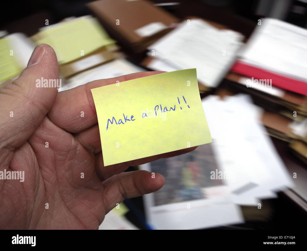 Messy office with hand holding note saying Make a Plan Stock Photo