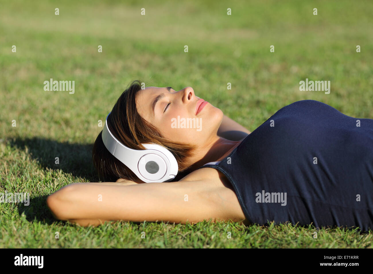 Relaxed woman listening to the music with headphones lying on the grass ...