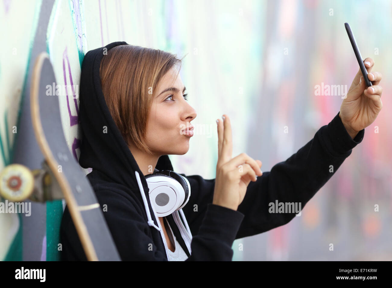 Skater teenager girl taking a photograph with smart phone camera with blurred graffiti wall in the background Stock Photo