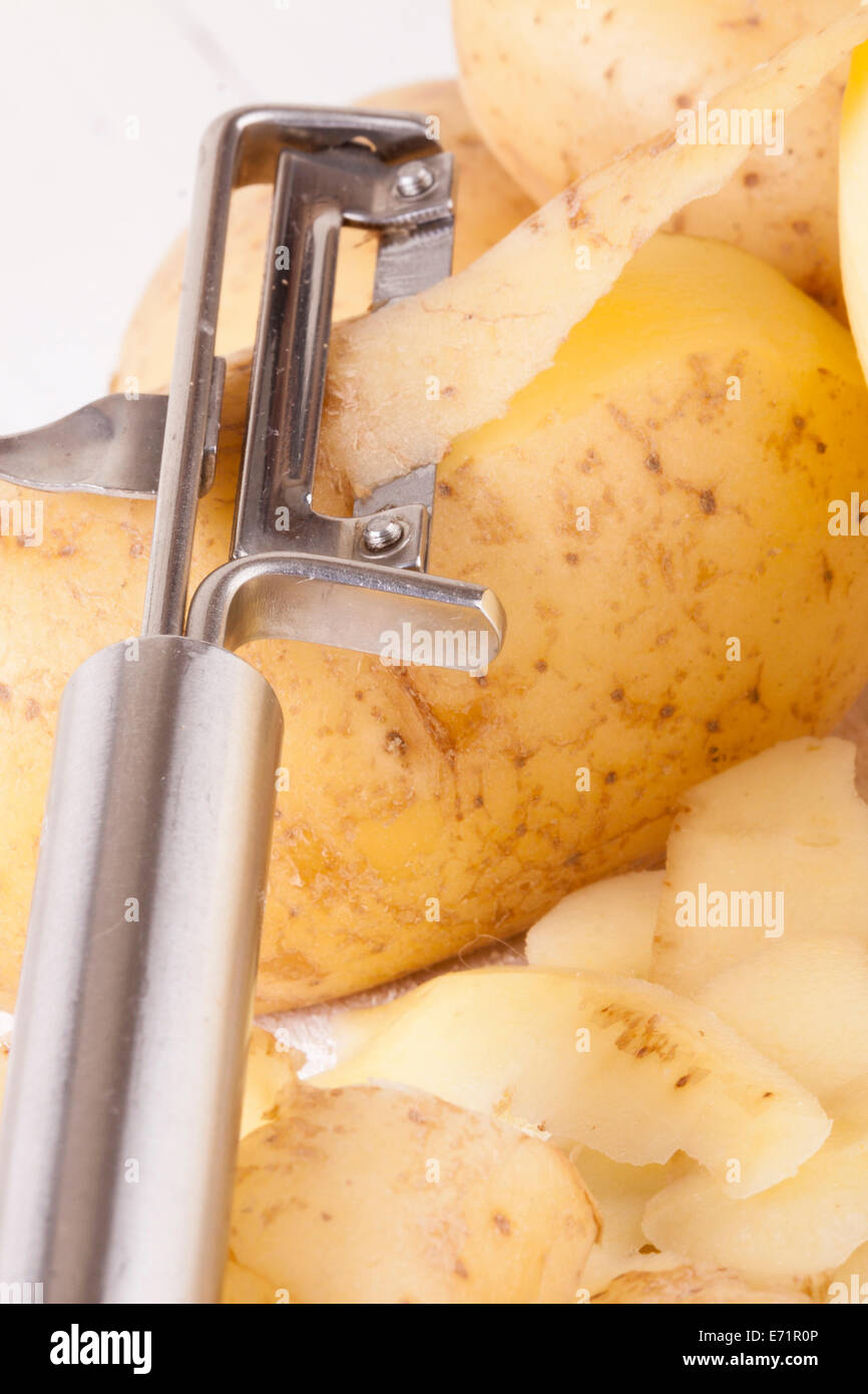 https://c8.alamy.com/comp/E71R0P/potatoes-with-peeler-and-peeled-skin-on-white-wooden-background-E71R0P.jpg