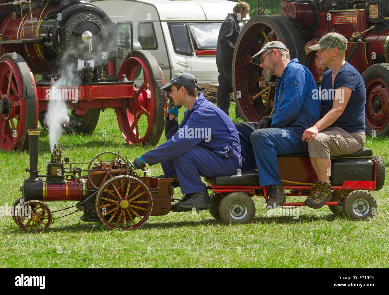 Three men riding on trailer pulled by miniature steam operated traction engine Stock Photo