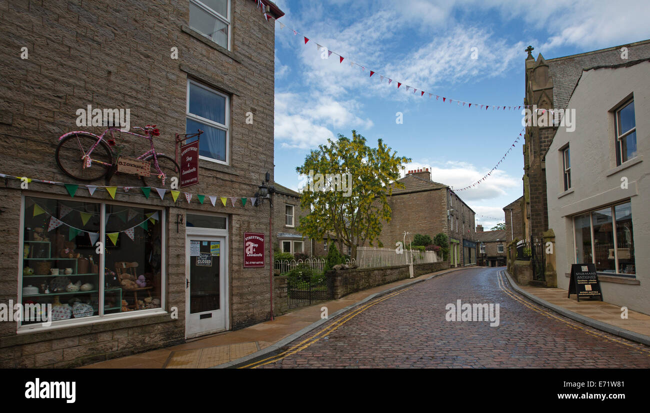 Narrow cobbled street winding between old shops and other buildings in English village of Hawes in Yorkshire, England Stock Photo