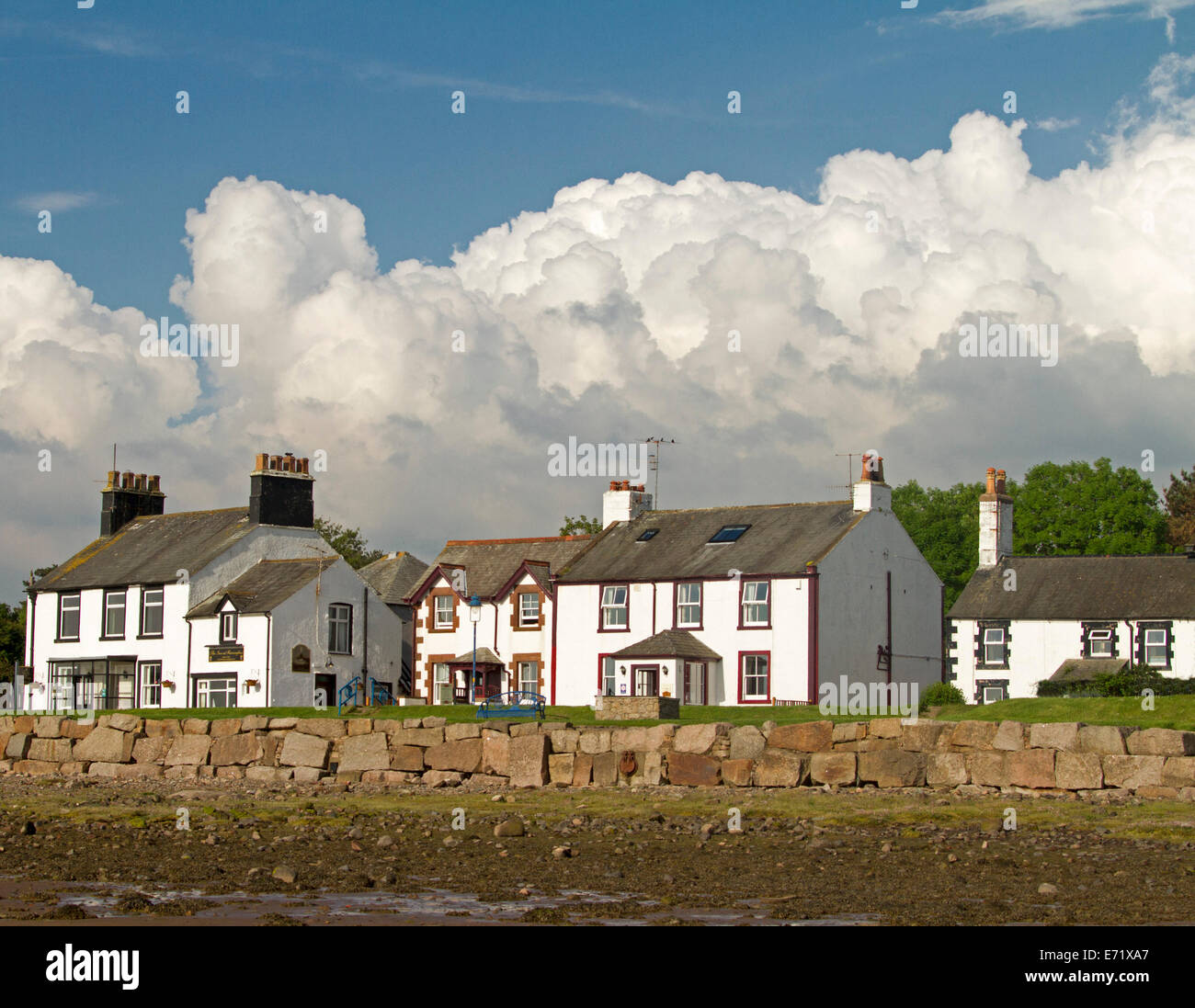 Traditional beachfront houses and sea wall with storm clouds in blue sky at coastal village of Ravenglass, Cumbria, England Stock Photo