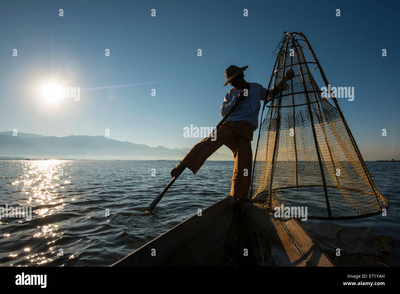 Fisherman in the morning light, leg rower with a traditional basket on the canoe, at sunrise, Inle Lake, Shan State, Myanmar Stock Photo