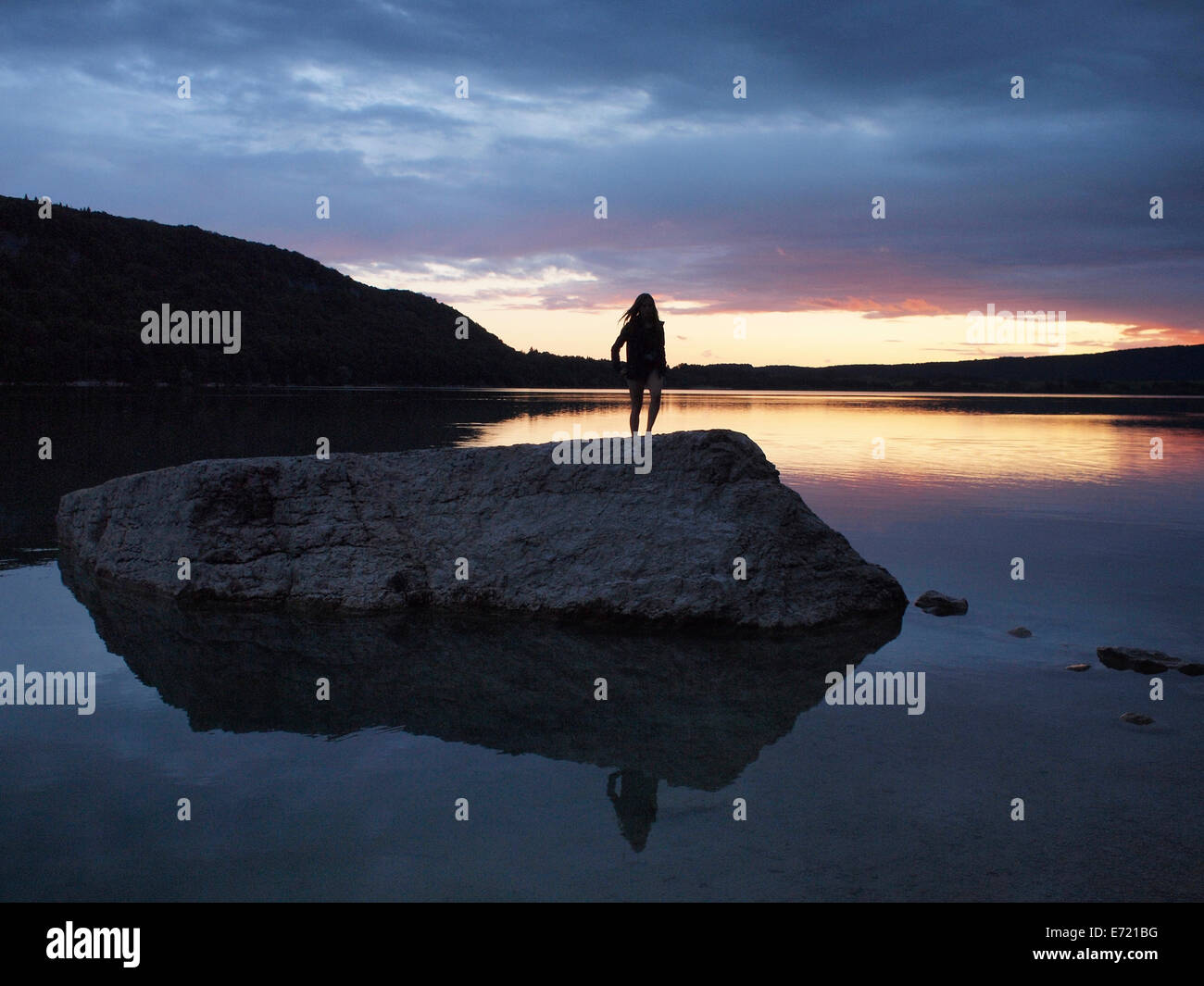 Lac de Chalain sunset, Jura, France with silhouetted person standing on a big rock. Stock Photo