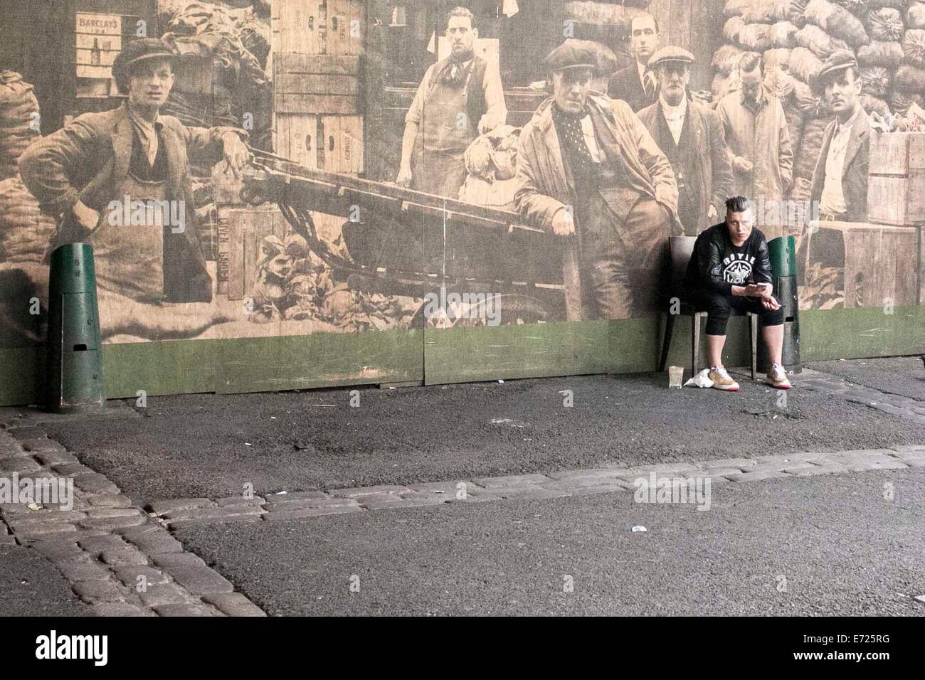 Borough Market , London. A young man sits in front a large historical photo of the market. Stock Photo