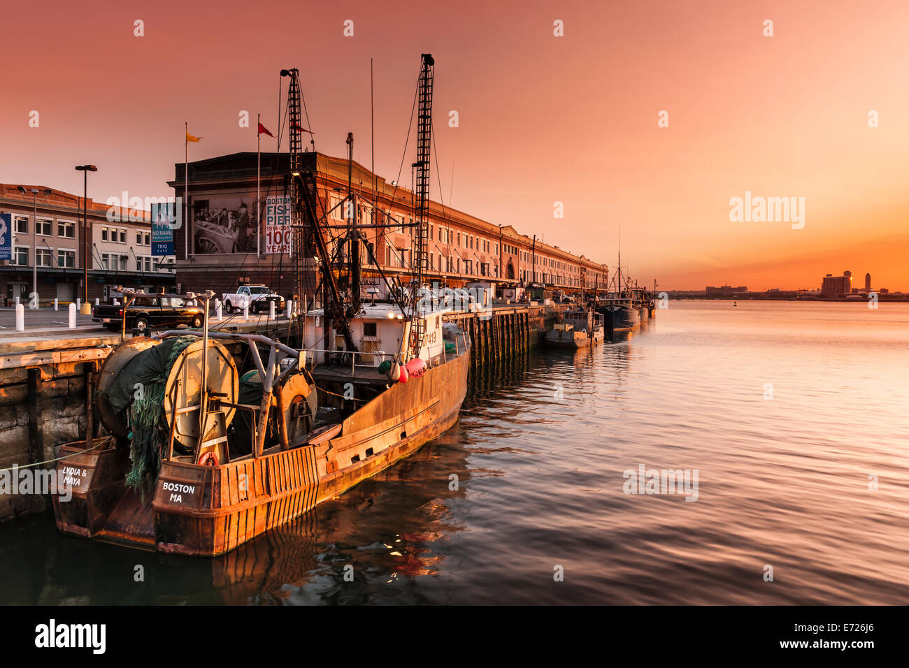 The sun rises over Logan International Airport, lighting up the fishing boats moored along the Fish Pier in the Seaport district Stock Photo