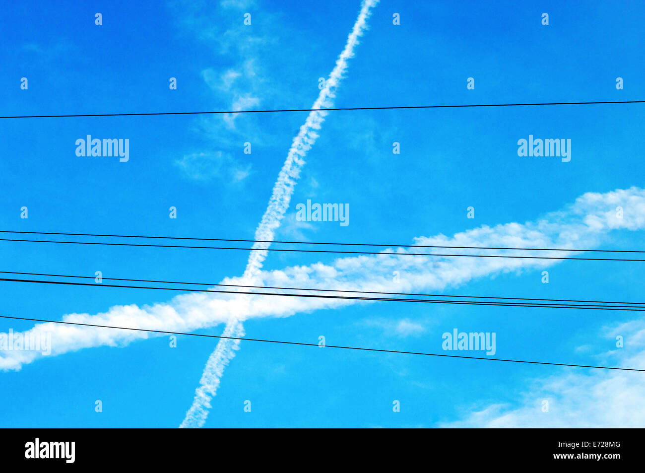 Vapor trails and telephone wires against blue sky Stock Photo