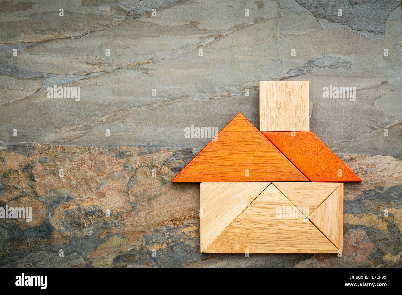 abstract picture of a house built from seven tangram wooden pieces against slate rock background Stock Photo