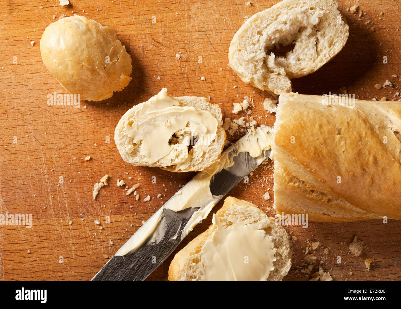 French bread baguette and its slices with butter and metal knife on wooden background. Stock Photo