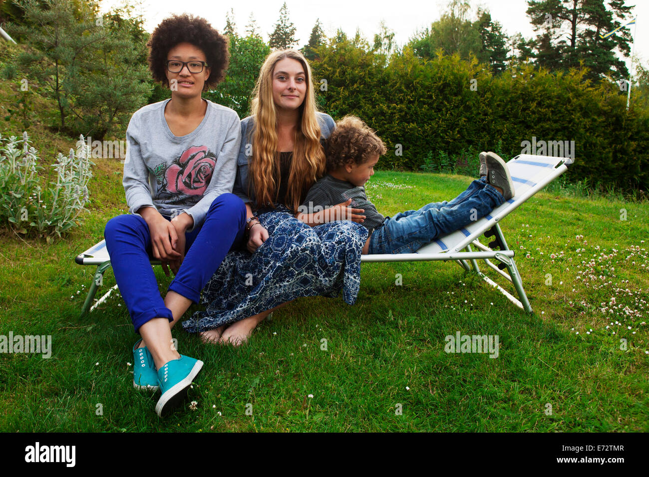 View of teenage girls(13-15, 16-17) and boy (2-3) on deckchair Stock Photo