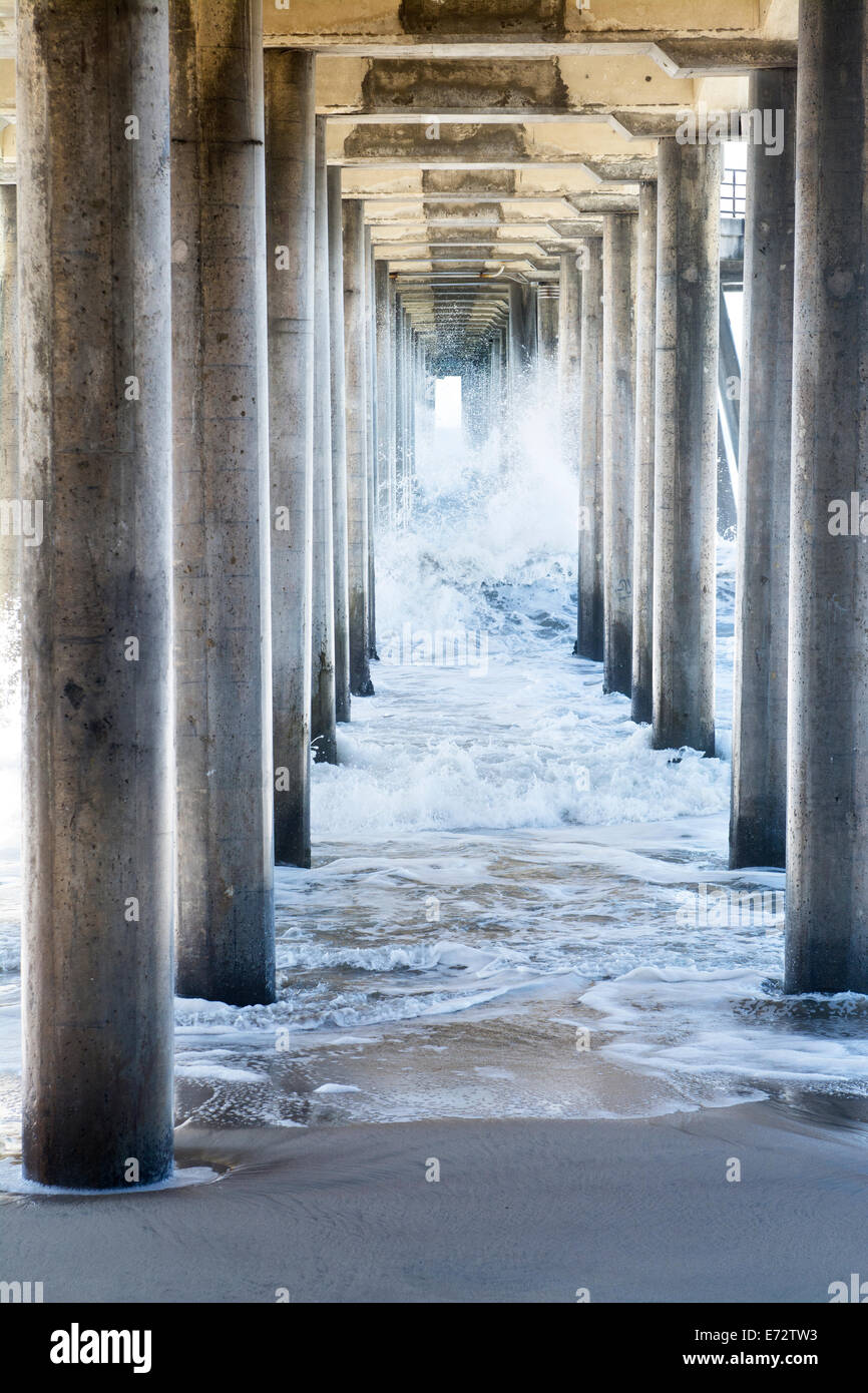 Waves generated by a storm rush through the underside of a pier, creating rough, turbulent water as it moves through the pillars Stock Photo