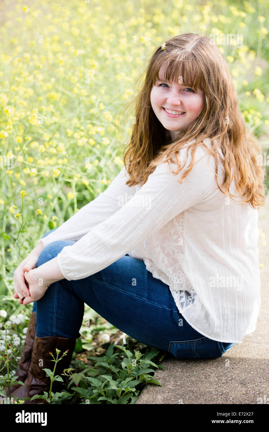 Portrait of teenage girl (13-15) sitting on wall in meadow Stock Photo