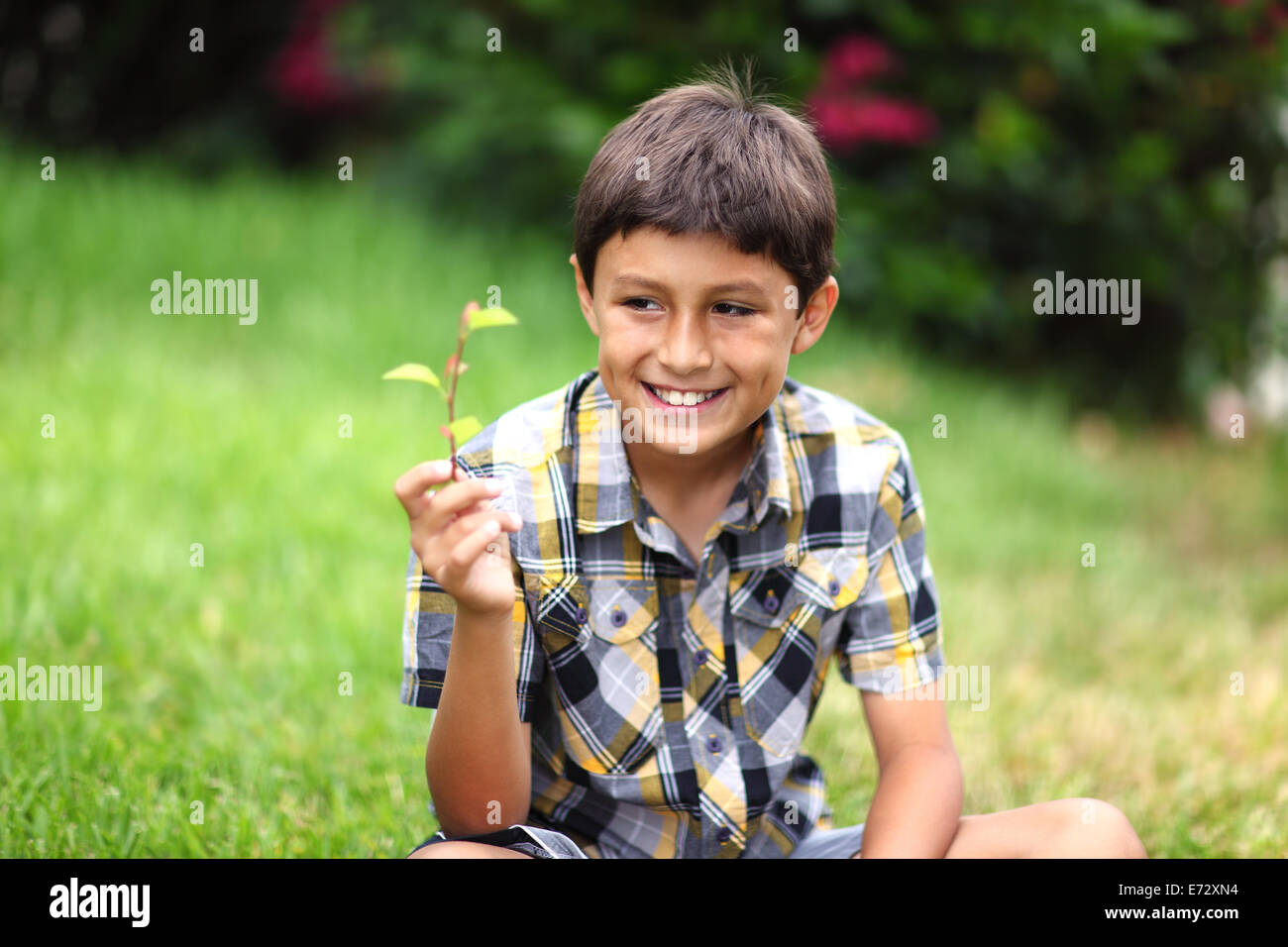 A young boy smiles as he looks at a flowering plant Stock Photo