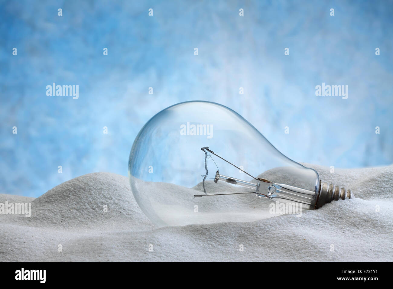 electric lamp bulb  on sand and light blue background Stock Photo