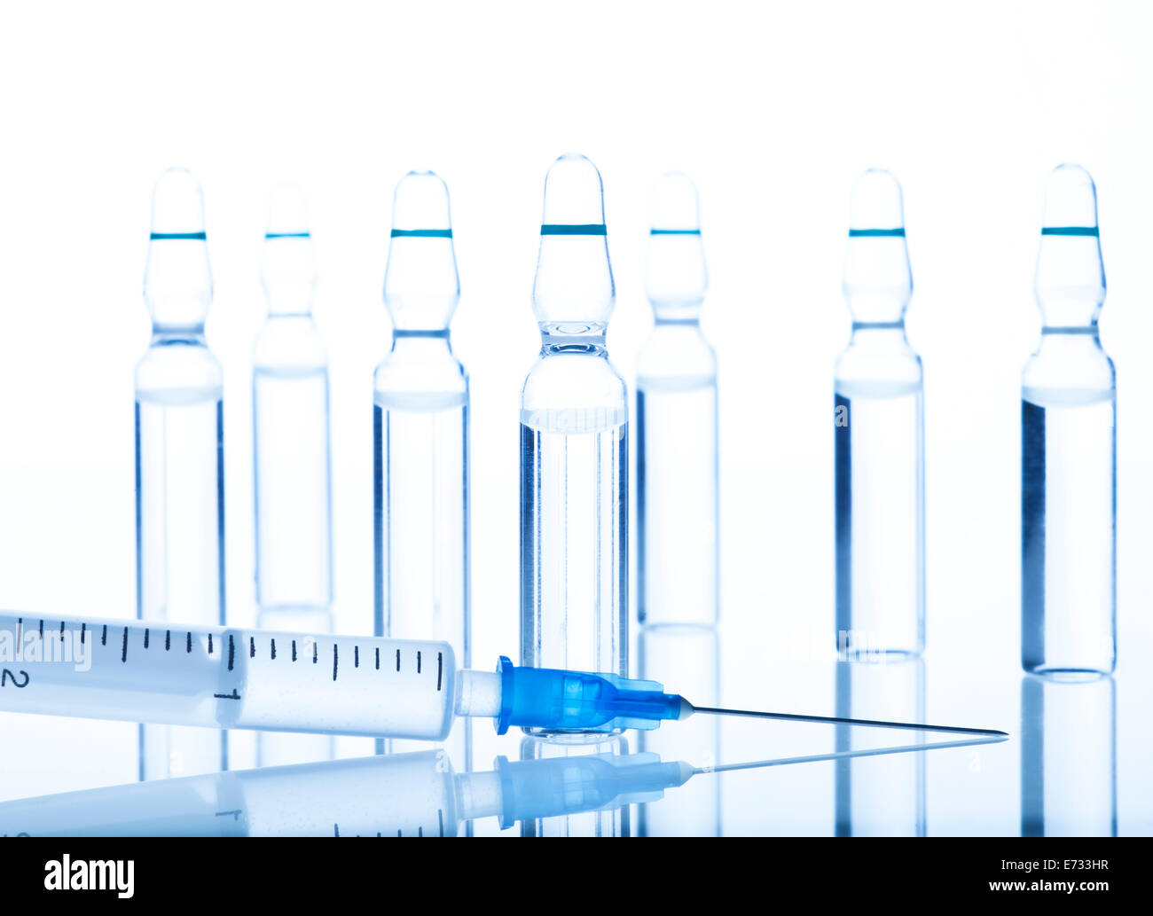 Glass Medicine Ampoules with liquid and Syringe on a white and blue background. Stock Photo