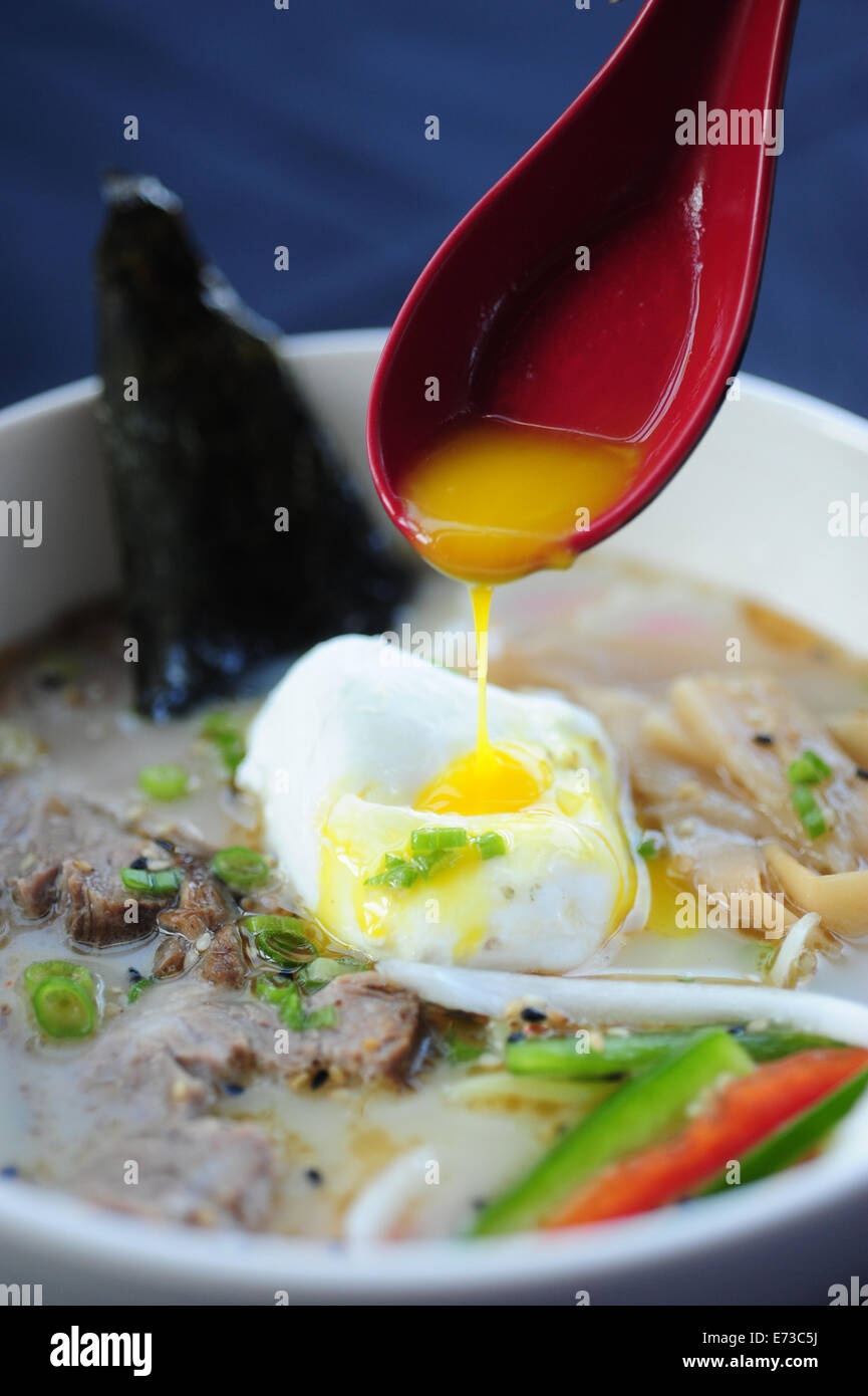 Food Dining Asian Japanese ramen noodle soup with an poached egg hand holding red spoon Stock Photo