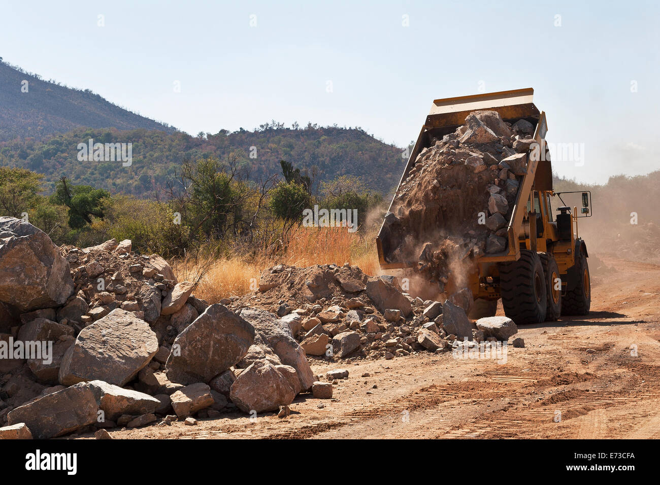 Dump truck tipping rocks during construction of access road to new platinum mine. South Africa Stock Photo