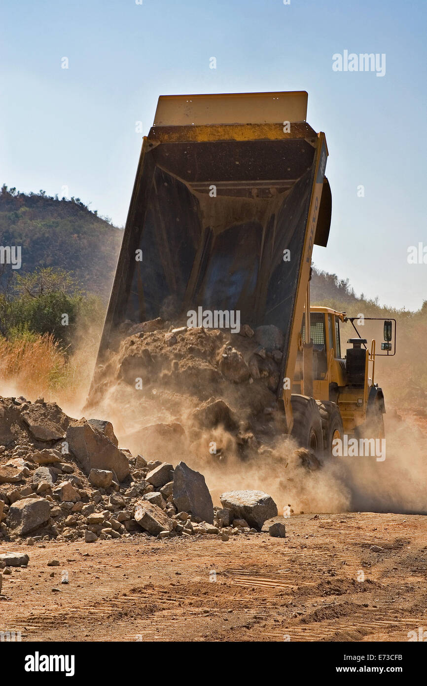 Dump truck tipping rocks during construction of access road to new platinum mine. South Africa Stock Photo