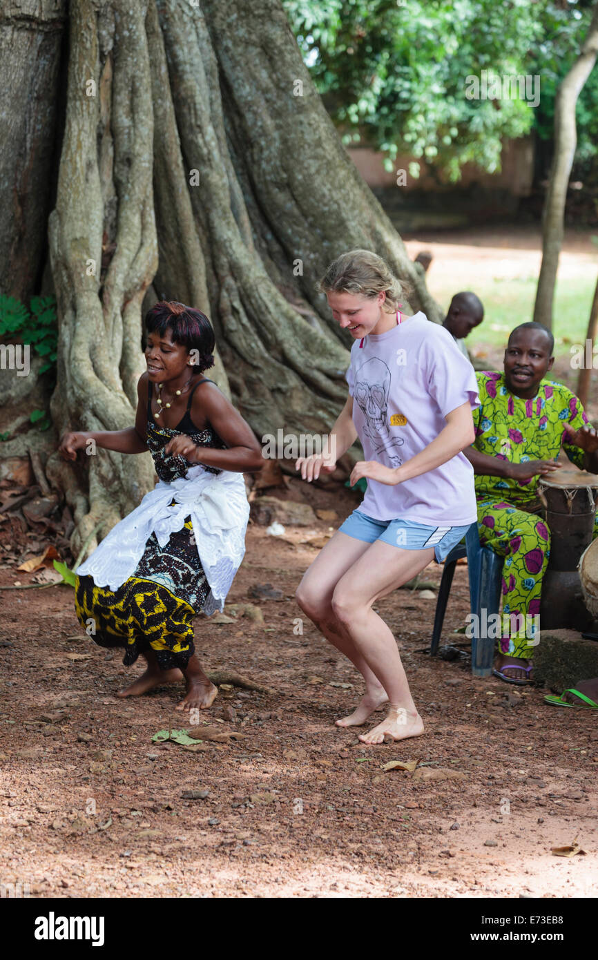 Africa, Benin, Ouidah. Local woman dancing with tourist during voodoo dance in front of iroko tree in Kpasse Sacred Forest. Stock Photo