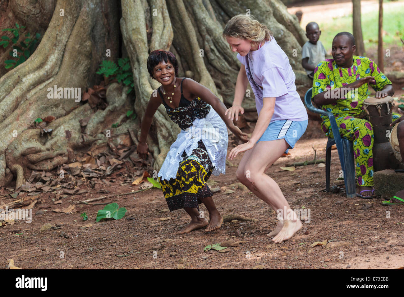 Africa, Benin, Ouidah. Local woman dancing with tourist during voodoo dance in front of iroko tree in Kpasse Sacred Forest. Stock Photo