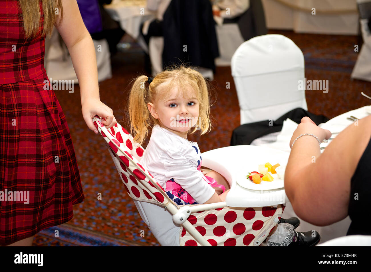 Bridesmaid Little girl sitting in highchair at a wedding reception enjoying meal Stock Photo