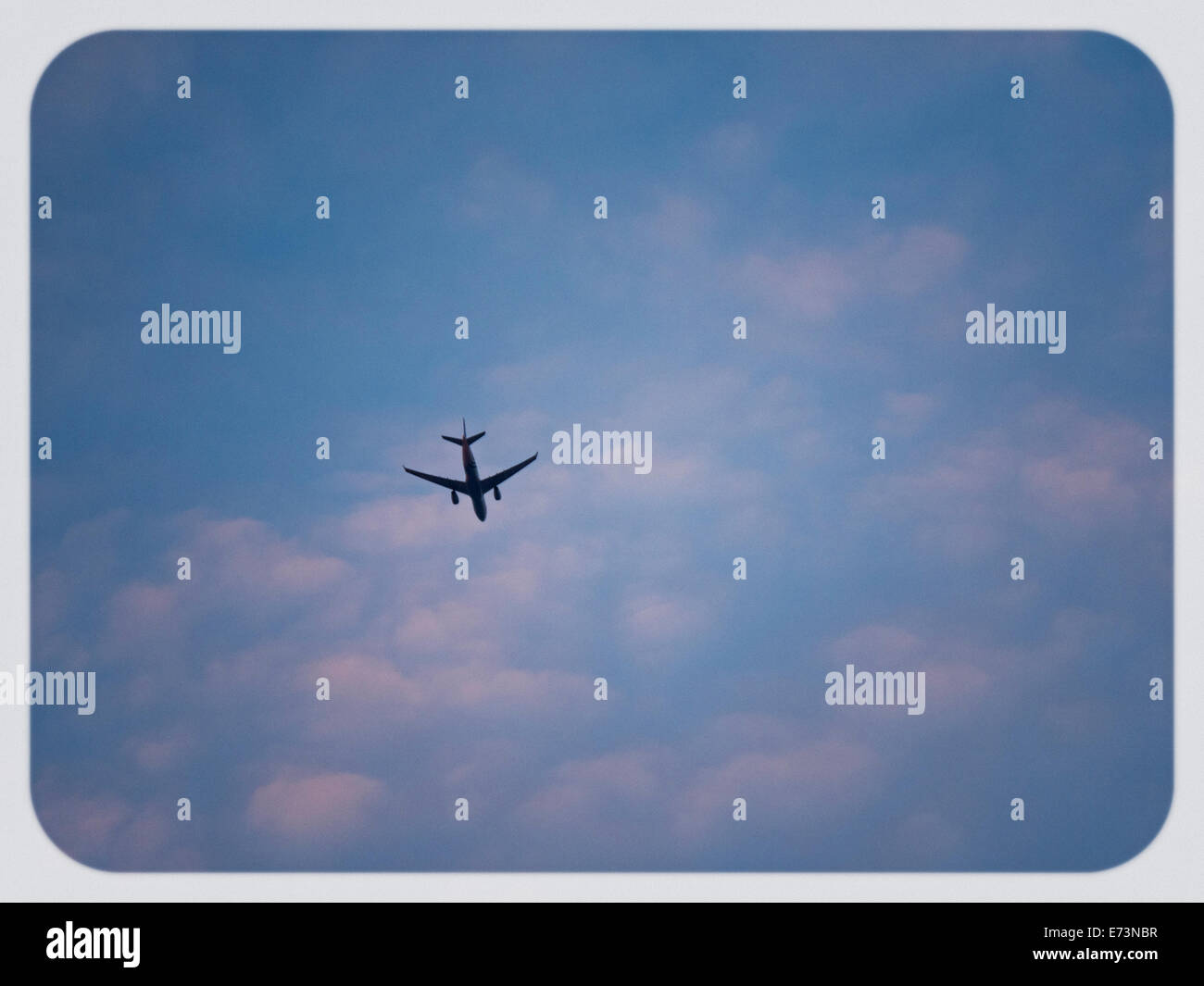 passenger jet flying overhead sunset colors on clouds Stock Photo