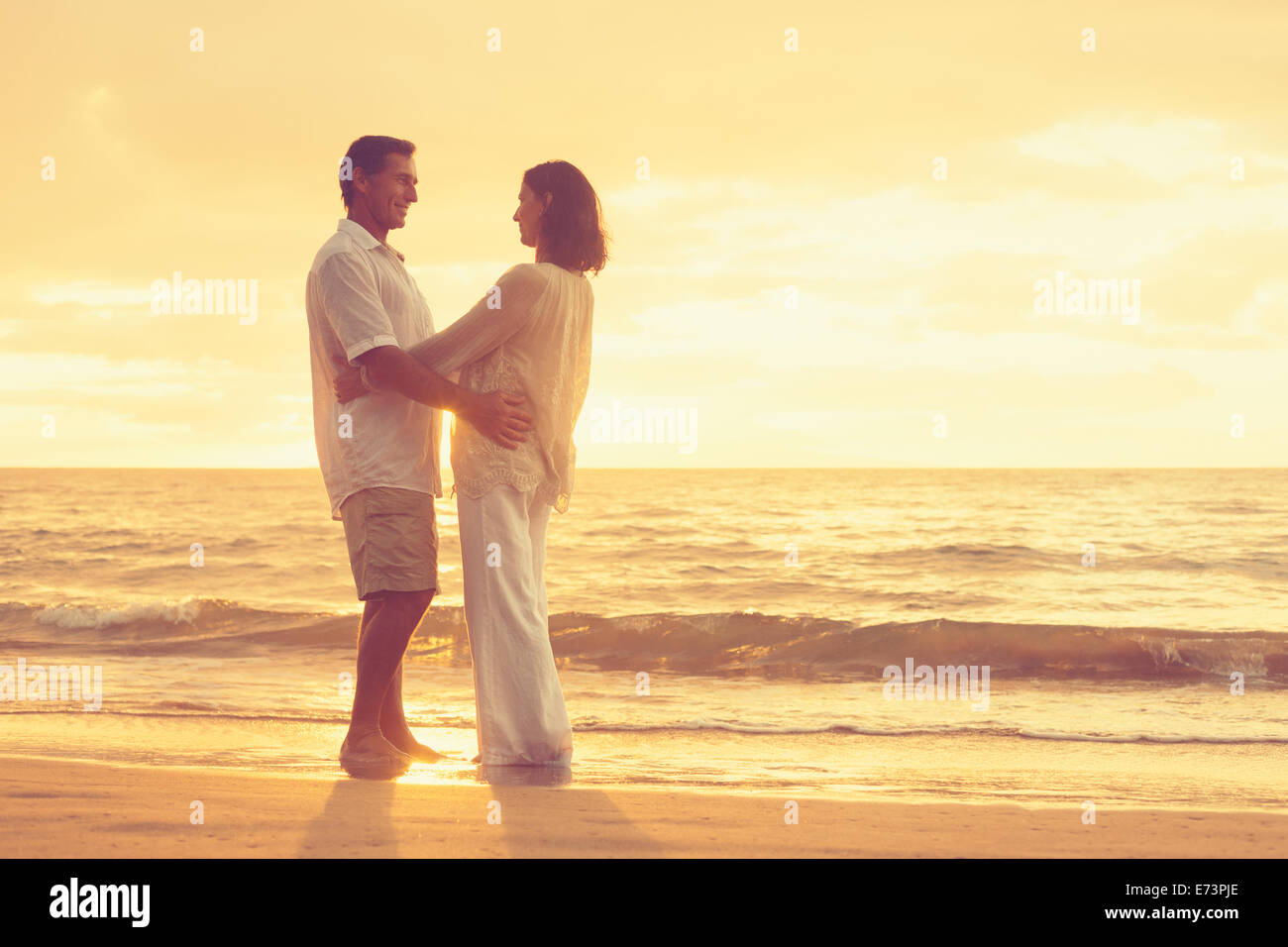 Romantic Retired Couple Relaxing on Beach Vacation at Sunset Stock Photo