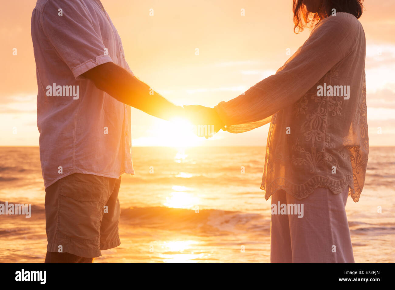 Romantic Mature Senior Couple Holding Hands Enjoying at Sunset on the Beach Stock Photo