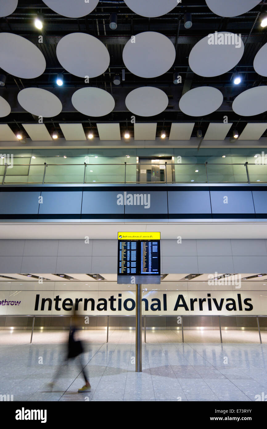 England, London, Heathrow Airport, International Arrivals hall in Terminal 5 with person walking past arrivals board. Stock Photo