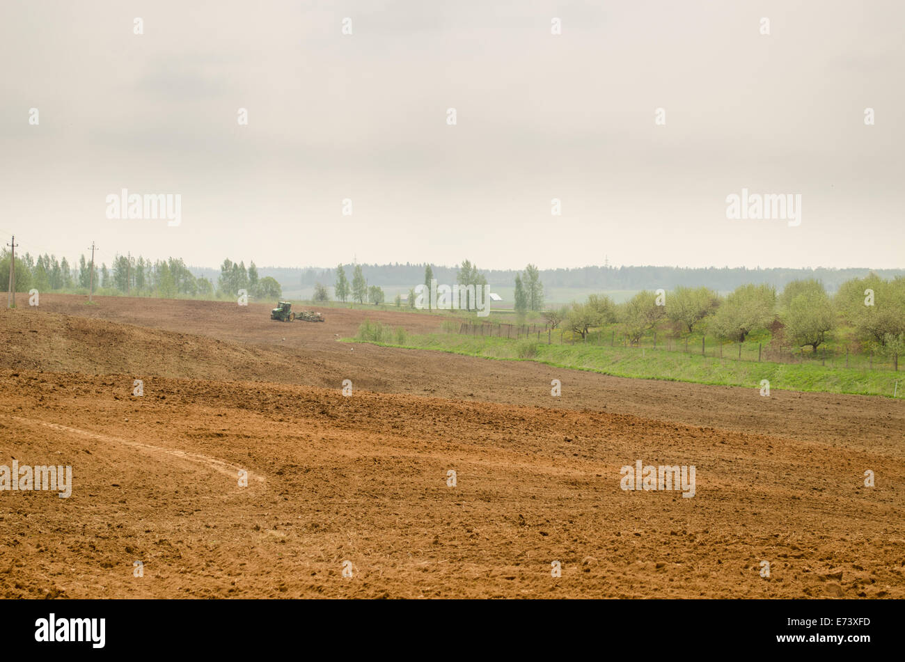 wide big brown plowed field in rural image with tractor in the distance Stock Photo