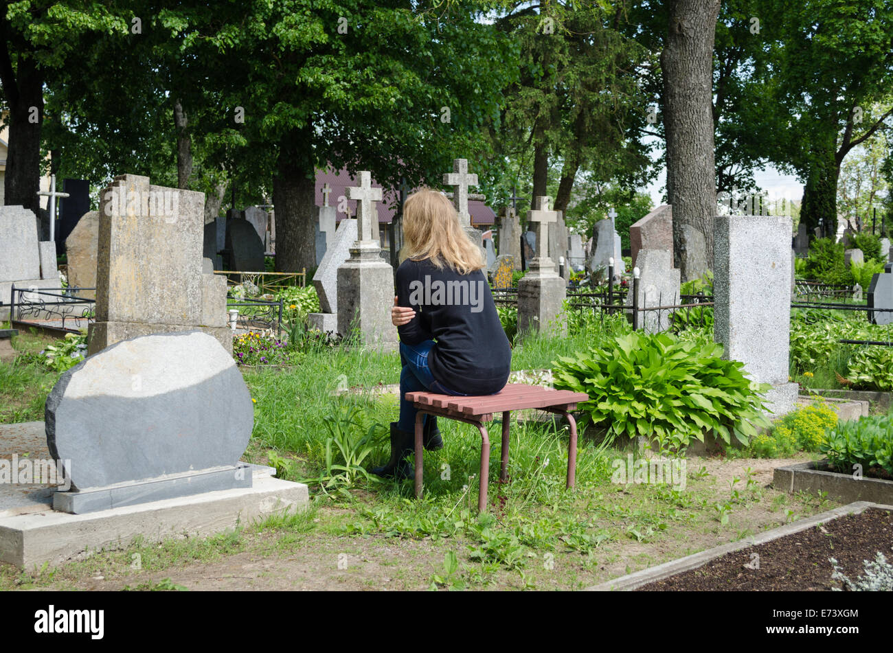 Sorrow woman shrinked near father husband tomb in graveyard. Stock Photo