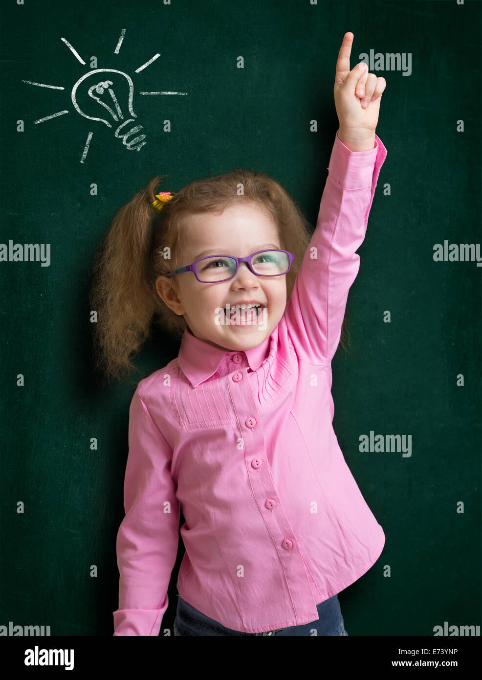 Happy kid girl in glasses with bright idea standing near school blackboard in classroom Stock Photo